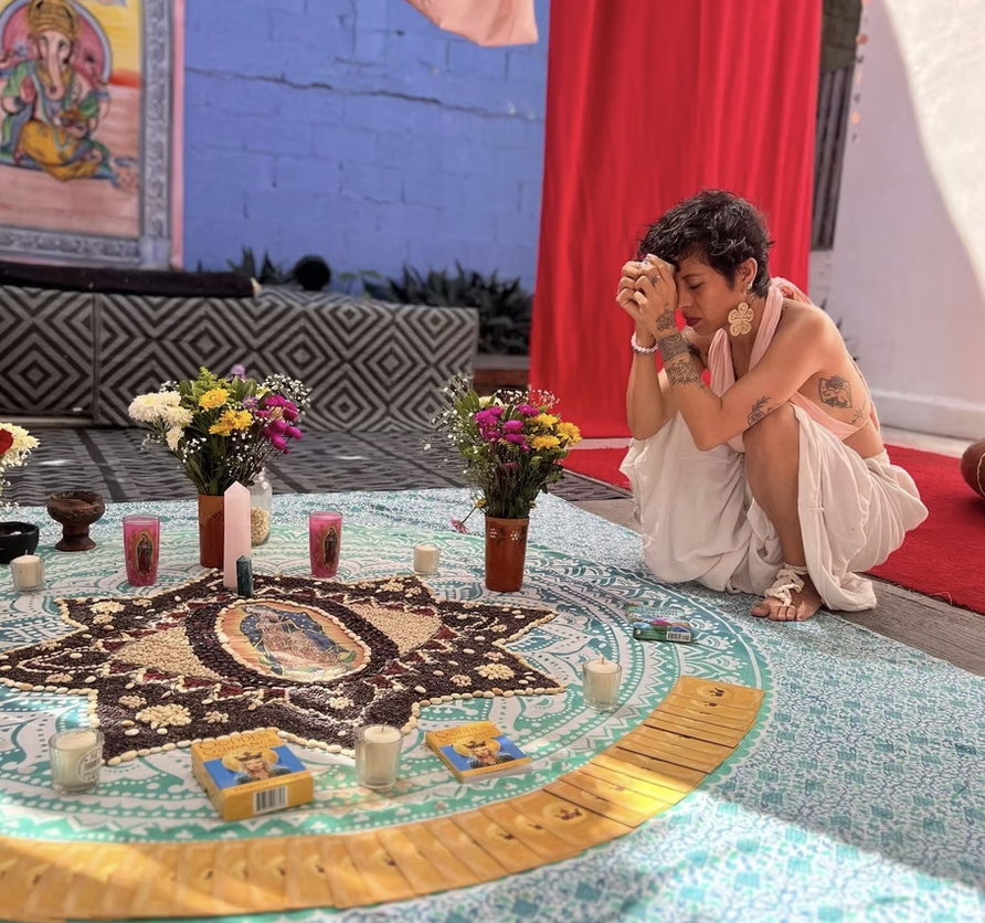 A woman in prayer beside a mandala altar of flowers and candles