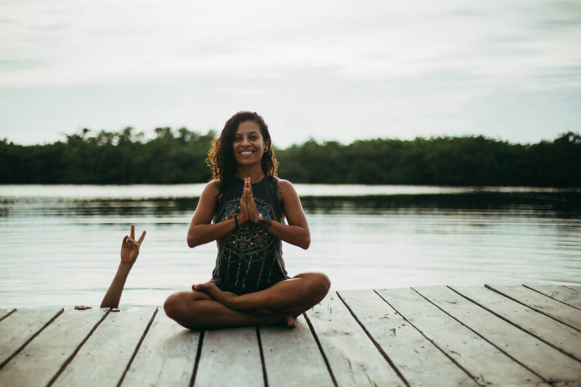 Luz meditating with palms together on a wooden dock by the lagoon
